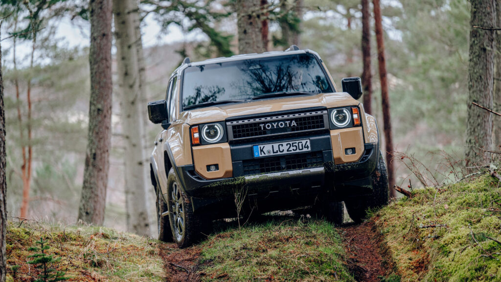Fundo de tela do novo Toyota Land Cruiser 2024 na cor bege (Sand), subindo um barranco de terra em uma trilha de floresta.