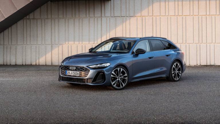 Fundo de tela de uma perua (station wagon) de luxo Audi A6 Avant, na cor azul-acinzentada, estacionada em um ambiente urbano moderno.