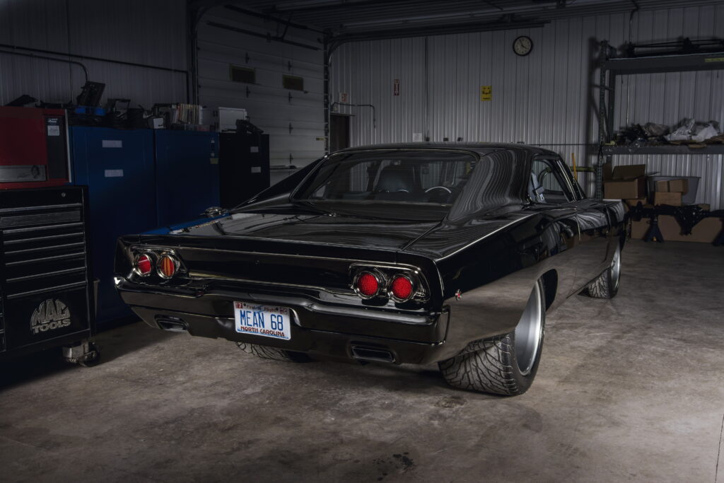 Fundo de tela de um Dodge Charger 1968 restomod, pintado de preto brilhante, visto de trás dentro de uma garagem de customização.
