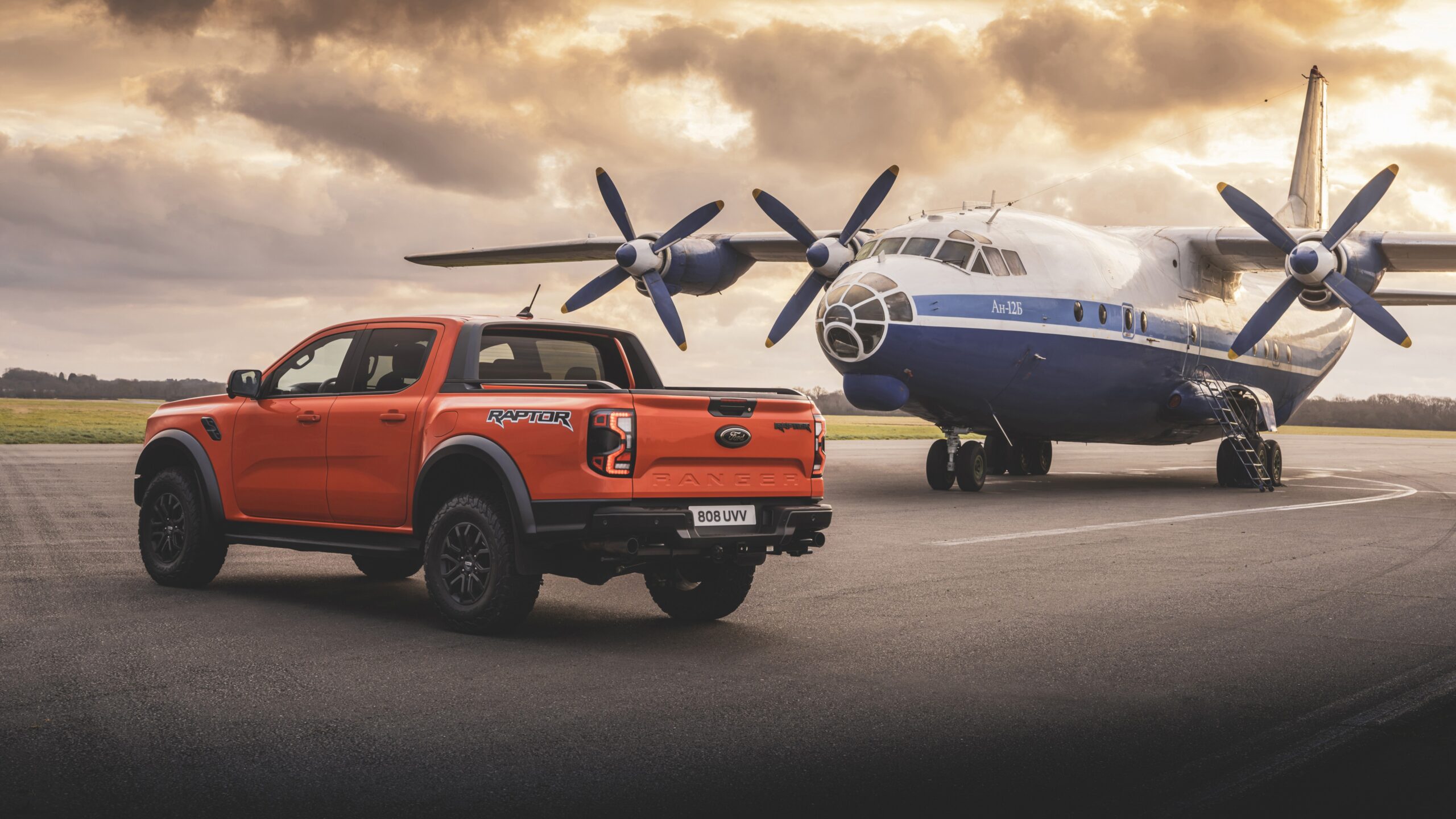Ford Ranger Raptor Laranja Papel de parede da nova picape Ford Ranger Raptor na cor laranja (Code Orange), estacionada em uma pista de aeroporto ao lado de um avião de carga.