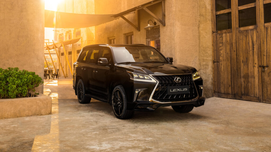 Fundo de tela de um SUV de luxo Lexus LX 570 preto (Black Edition), estacionado em um pátio com arquitetura árabe/deserto ao pôr do sol.