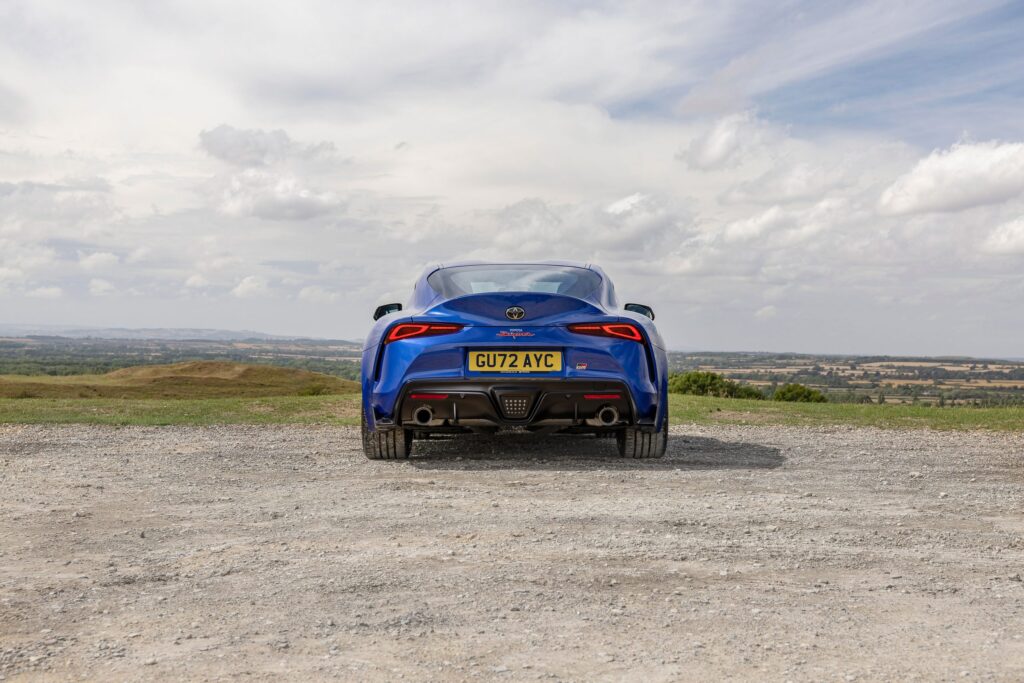 Fundo de tela da traseira do Toyota GR Supra (A90) azul, estacionado em um mirante de cascalho no interior (Reino Unido).