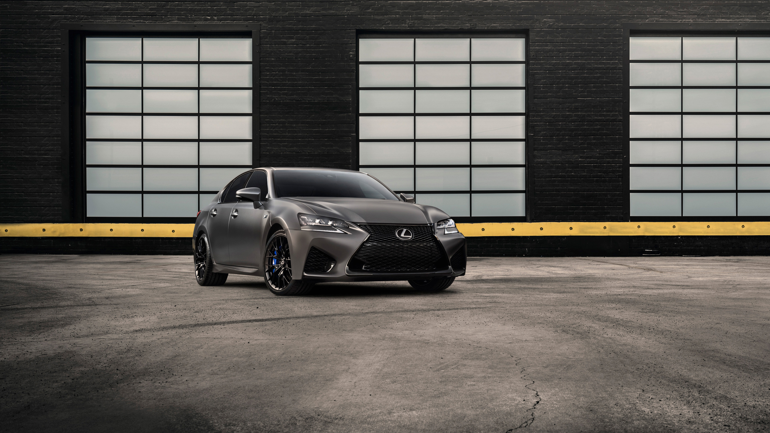 Lexus GS F Papel de parede de um sedan esportivo Lexus GS F na cor cinza fosco (Nebula Gray), estacionado em um pátio industrial com janelas ao fundo.